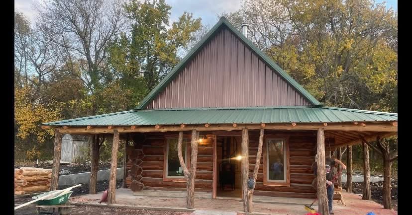 Completed full-log cedar cabin with green metal roof and wrap-around porch